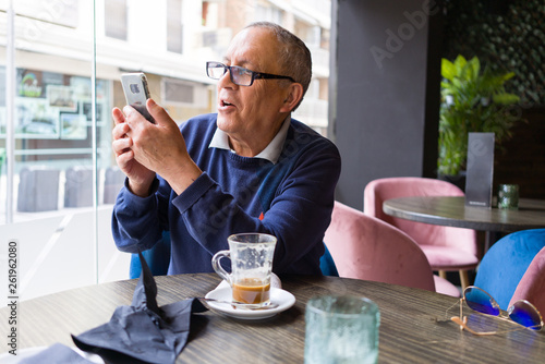 Handsome middle age senior man drinking coffee at restaurante, smiling happy enjoying and relaxing retirement using smartphone
