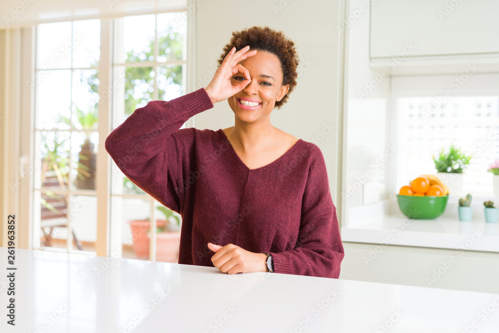 Young beautiful african american woman at home doing ok gesture with hand smiling, eye looking through fingers with happy face. Young beautiful african american woman at home doing ok gesture with hand smiling, eye looking through fingers with happy face.