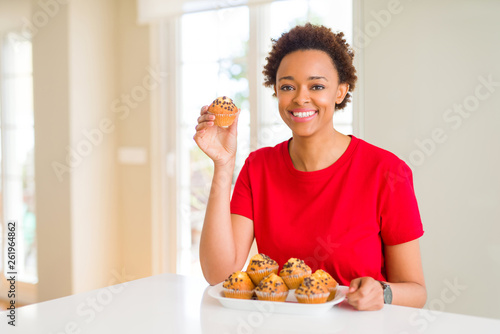 Young african american woman eating chocolate chips muffins with a happy face standing and smiling with a confident smile showing teeth