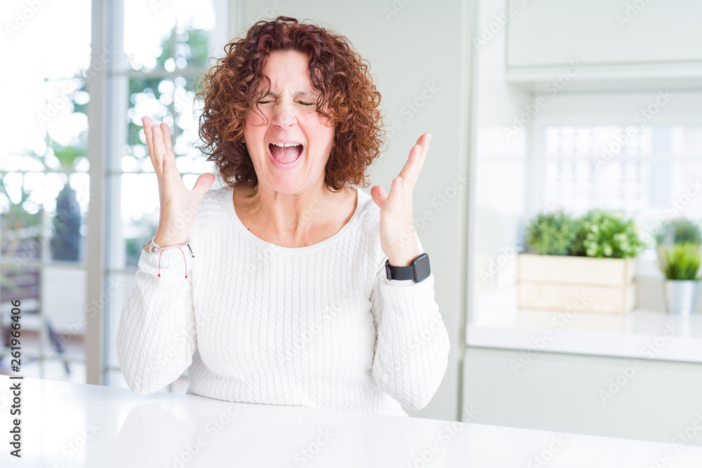Beautiful senior woman wearing white sweater at home celebrating mad and crazy for success with arms raised and closed eyes screaming excited. Winner concept Beautiful senior woman wearing white sweater at home celebrating mad and crazy for success with arms raised and closed eyes screaming excited. Winner concept
