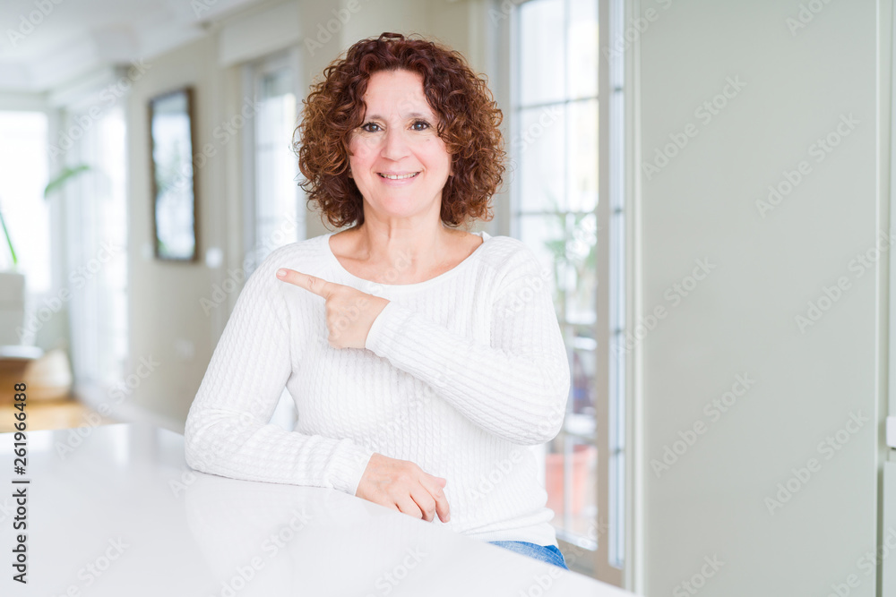 Beautiful senior woman wearing white sweater cheerful with a smile of face pointing with hand and finger up to the side with happy and natural expression on face Beautiful senior woman wearing white sweater cheerful with a smile of face pointing with hand and finger up to the side with happy and natural expression on face