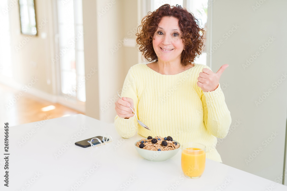 Senior woman eating healthy breakfast in the morning at home pointing and showing with thumb up to the side with happy face smiling Senior woman eating healthy breakfast in the morning at home pointing and showing with thumb up to the side with happy face smiling