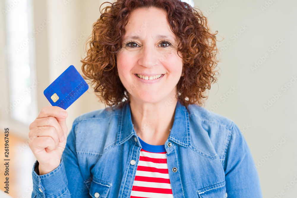 Senior woman holding credit card as payment with a happy face standing and smiling with a confident smile showing teeth Senior woman holding credit card as payment with a happy face standing and smiling with a confident smile showing teeth