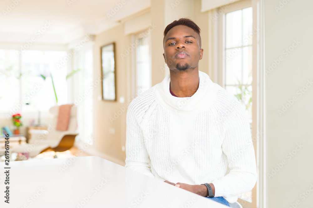 Handsome african american man on white table with serious expression on face. Simple and natural looking at the camera.