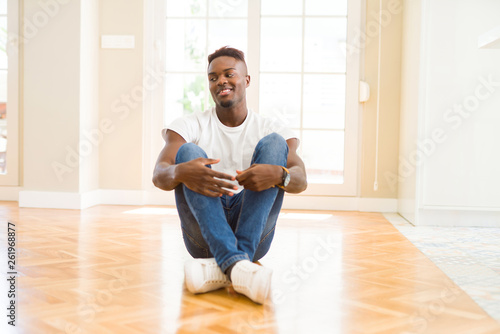 Handsome african american man sitting on the floor at home looking away to side with smile on face, natural expression. Laughing confident. © Krakenimages.com