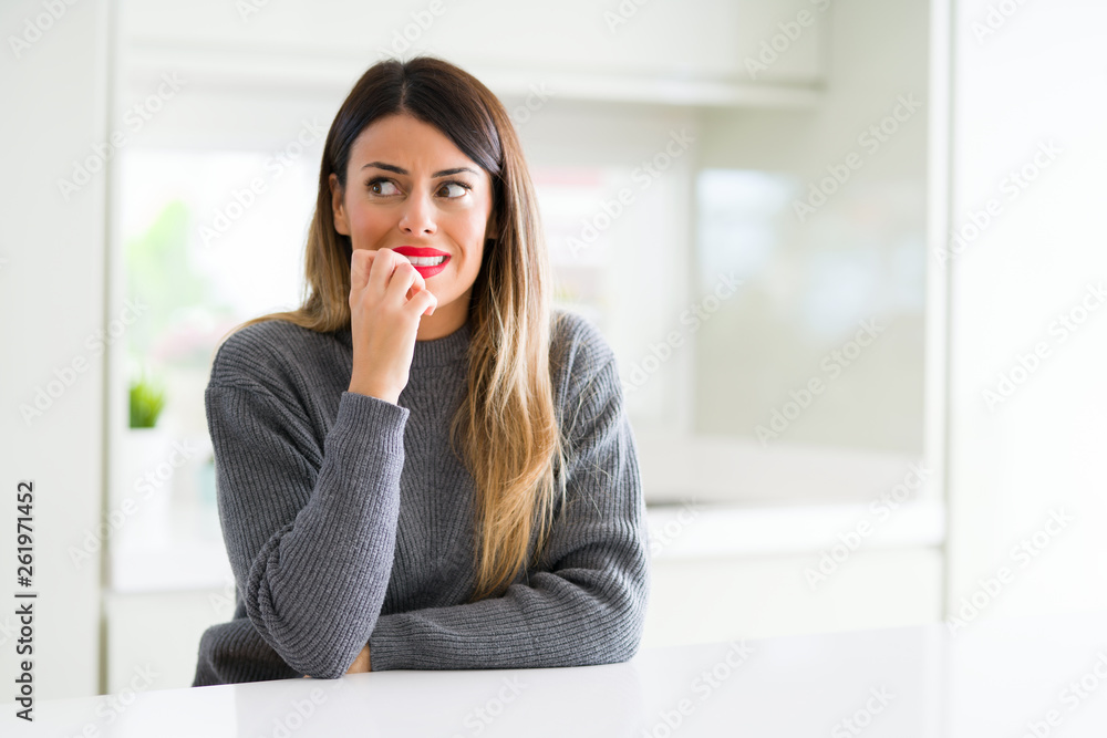 Young beautiful woman wearing winter sweater at home looking stressed and nervous with hands on mouth biting nails. Anxiety problem. Young beautiful woman wearing winter sweater at home looking stressed and nervous with hands on mouth biting nails. Anxiety problem.