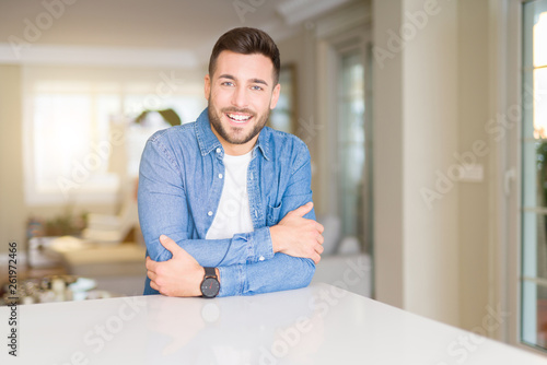 Young handsome man at home happy face smiling with crossed arms looking at the camera. Positive person.