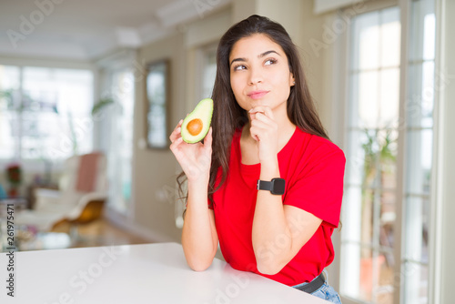 Young woman eating healthy avocado serious face thinking about question  very confused idea