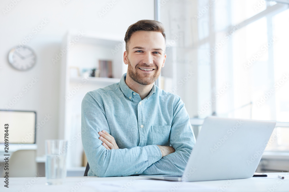 Portrait of handsome entrepreneur smiling happily at camera while posing at workplace in office, copy space Portrait of handsome entrepreneur smiling happily at camera while posing at workplace in office, copy space
