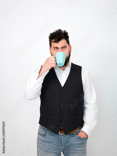 handsome, young man with black beard posing with turquoise coffee cup or tea cup in front of white background and making different facial expressions