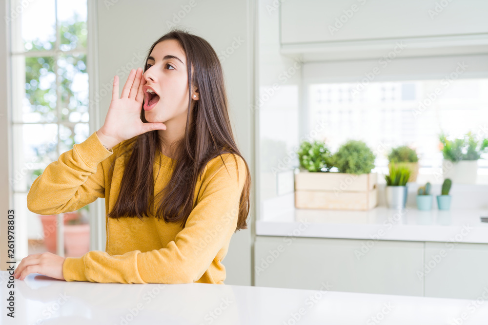 Beautiful young woman wearing yellow sweater shouting and screaming loud to side with hand on mouth. Communication concept. Beautiful young woman wearing yellow sweater shouting and screaming loud to side with hand on mouth. Communication concept.