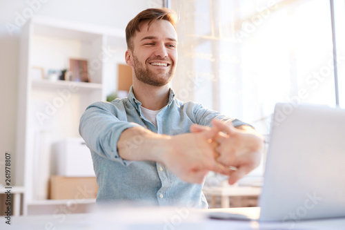 Portrait of handsome young man  stretching at workplace in office and smiling happily, copy space photo
