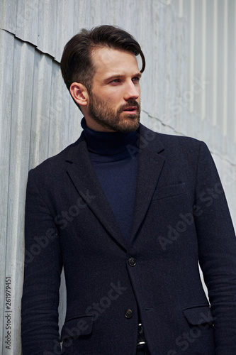 Fashion beard style business handsome male model posing in style clothing blue jacket on street wall outdoors background. Closeup