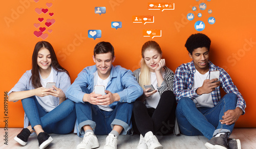 Teenagers with smartphones chatting in social networks, orange wall photo