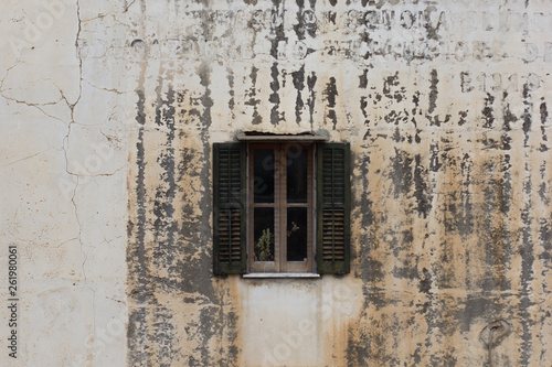 One small window with wooden shutters on aged and cracked wall with invisible inscription