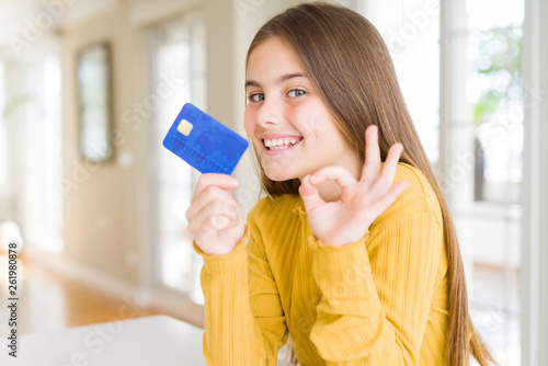 Beautiful young girl kid holding credit card doing ok sign with fingers, excellent symbol