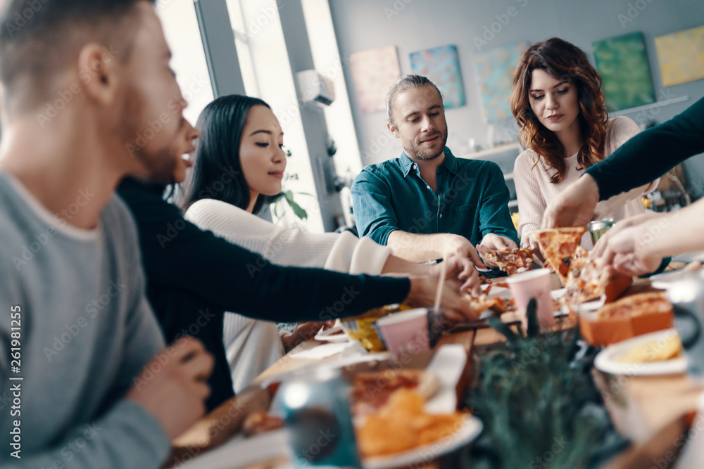 Obraz premium Wybór najlepszego plastra. Grupa młodych ludzi w casual zbierając pizzę i uśmiechając się podczas kolacji w pomieszczeniu