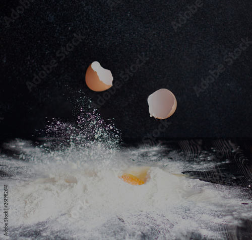 Eggs are broken and fall into flour on a black background.