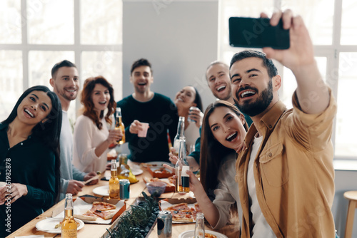 Capturing the moment. Group of young people in casual wear taking selfie and smiling while having a dinner party indoors