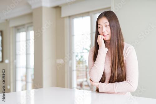 Beautiful Asian woman wearing casual sweater on white table looking stressed and nervous with hands on mouth biting nails. Anxiety problem.