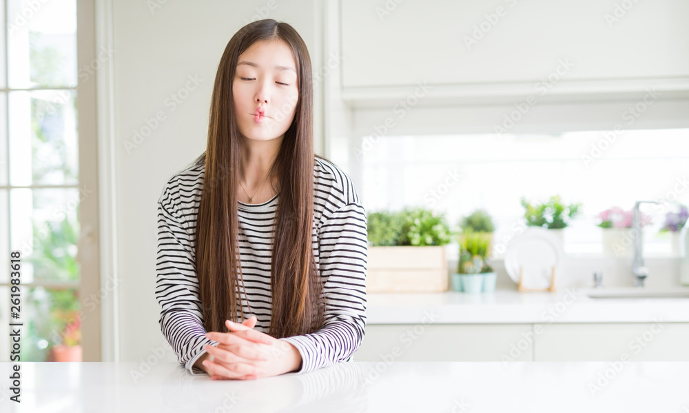 Beautiful Asian woman wearing stripes sweater making fish face with lips, crazy and comical gesture. Funny expression. Beautiful Asian woman wearing stripes sweater making fish face with lips, crazy and comical gesture. Funny expression.