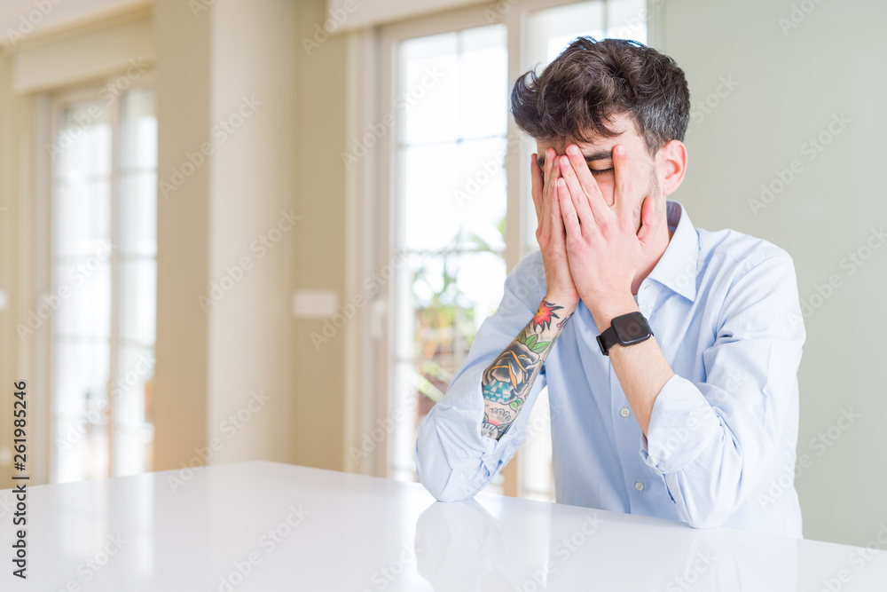 Young businesss man sitting on white table with sad expression covering face with hands while crying. Depression concept. Young businesss man sitting on white table with sad expression covering face with hands while crying. Depression concept.