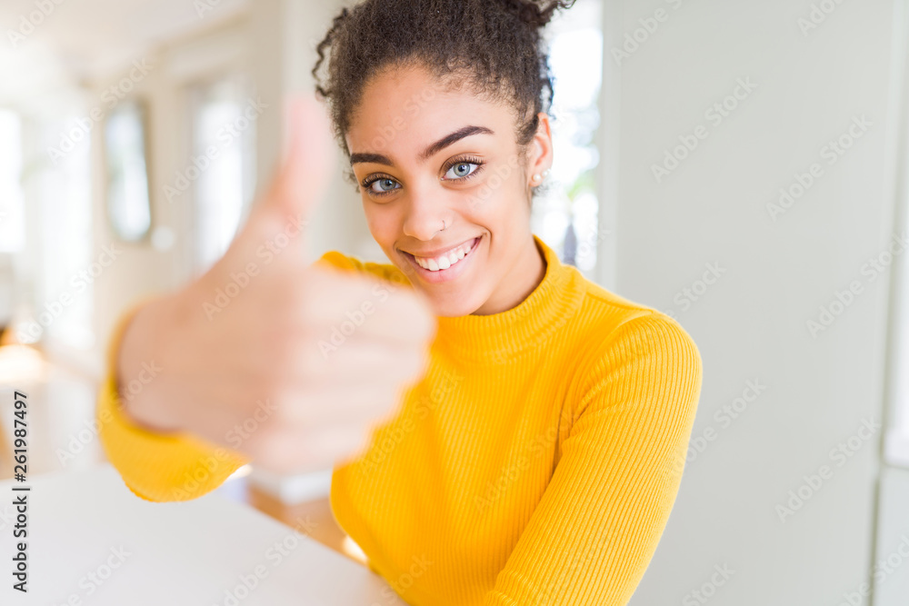 Beautiful young african american woman with afro hair doing happy thumbs up gesture with hand. Approving expression looking at the camera showing success. Beautiful young african american woman with afro hair doing happy thumbs up gesture with hand. Approving expression looking at the camera showing success.