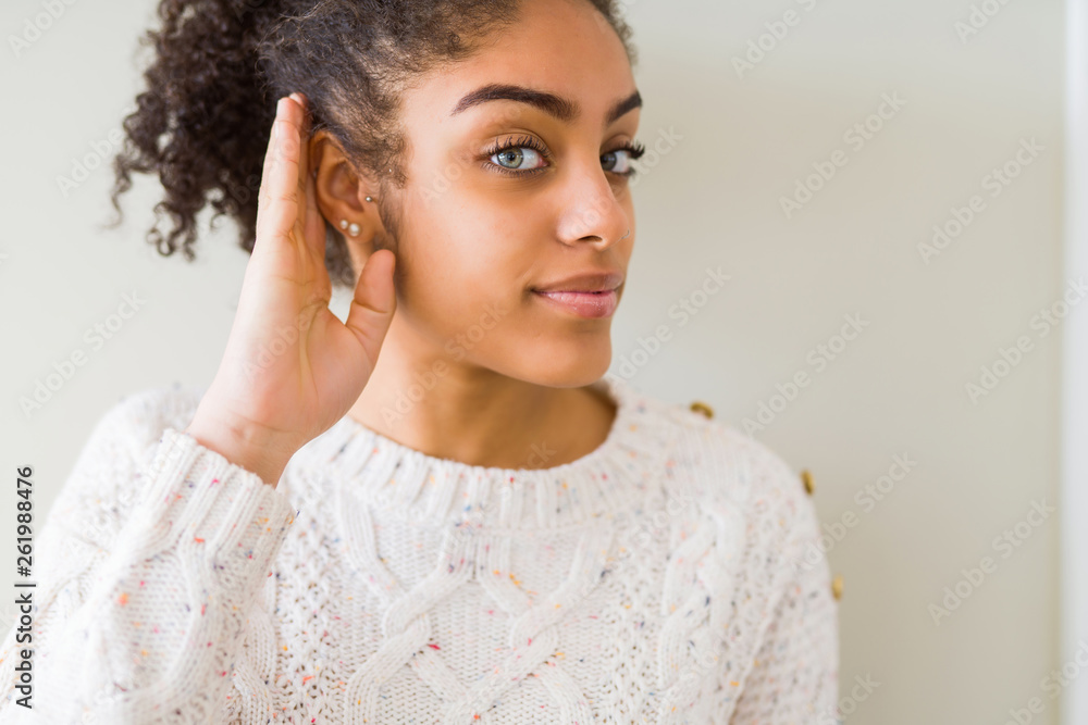 Beautiful young african american woman with afro hair wearing casual sweater smiling with hand over ear listening an hearing to rumor or gossip. Deafness concept. Beautiful young african american woman with afro hair wearing casual sweater smiling with hand over ear listening an hearing to rumor or gossip. Deafness concept.
