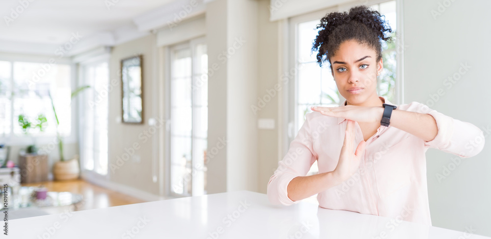 Wide angle of beautiful african american woman with afro hair Doing time out gesture with hands, frustrated and serious face