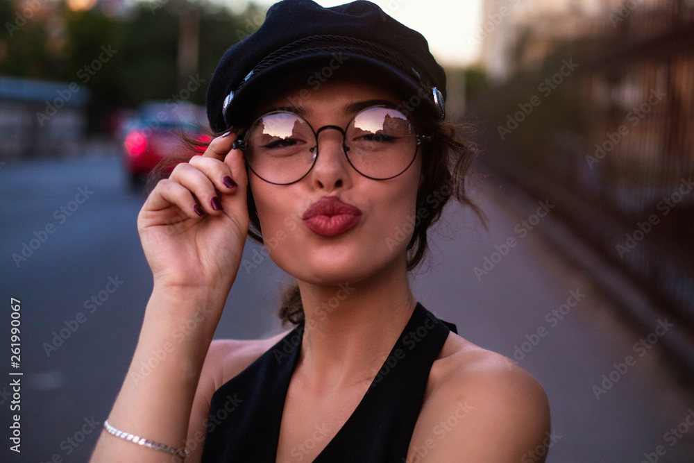 Portrait of cute lovely girl in casual outfit with modern hairdo sending blowing kiss with pout lips looking at camera at street background. Affection feelings concept Portrait of cute lovely girl in casual outfit with modern hairdo sending blowing kiss with pout lips looking at camera at street background. Affection feelings concept