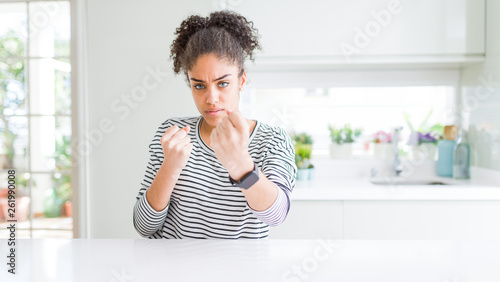 Beautiful african american woman with afro hair wearing casual striped sweater Ready to fight with fist defense gesture  angry and upset face  afraid of problem