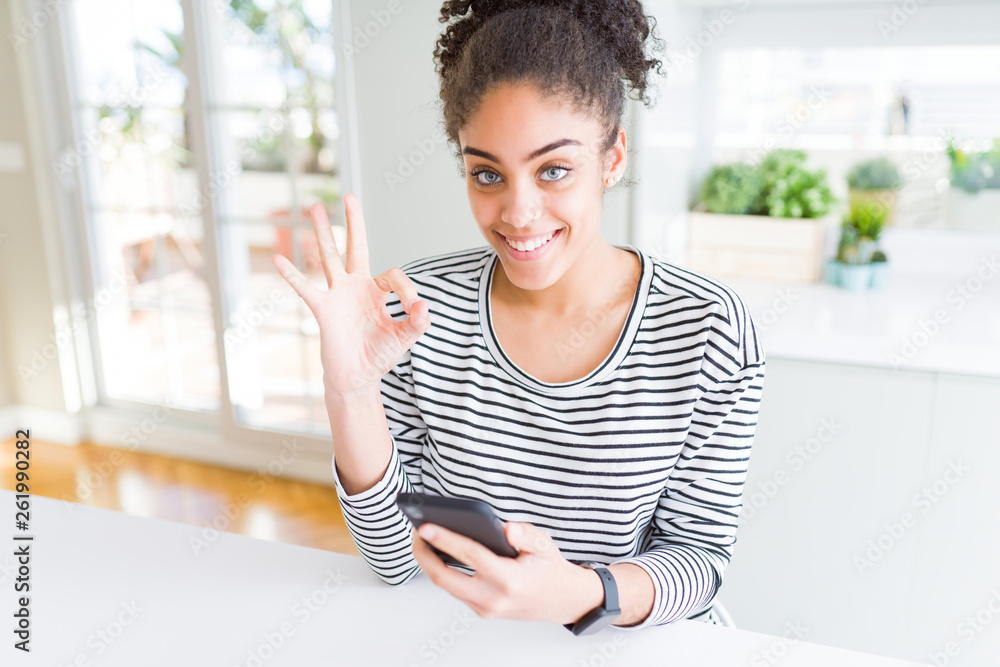 Young african american woman using smartphone texting a message doing ok sign with fingers, excellent symbol