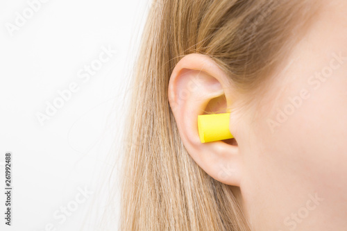 Yellow earplug into young woman's ear. Isolated on white background. Closeup. 