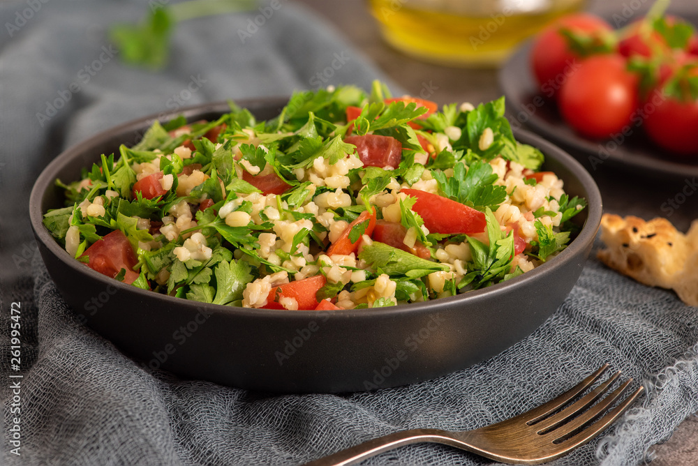 Tabbouleh salad with bulgur, parsley, spring onion and tomato in bowl on grey background. Top view. WIth copy space
