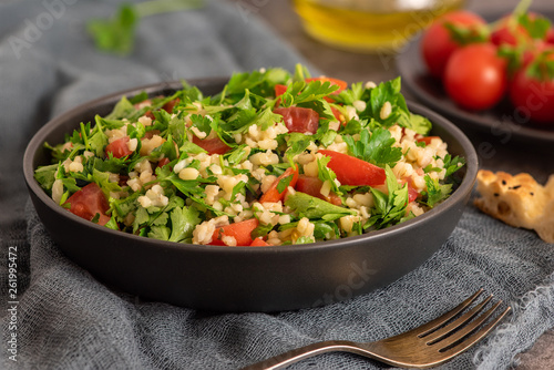 Tabbouleh salad with bulgur, parsley, spring onion and tomato in bowl on grey background. Top view. WIth copy space
