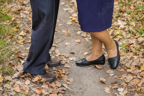 Closeup view of male and female legs of senior couple standing together outdoors in autumn park. Horizontal color photography.