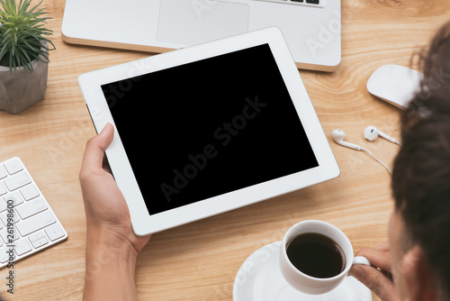 Fototapeta Naklejka Na Ścianę i Meble -  Mock up image of a hand holding black tablet pc with white blank screen and coffee cup on wooden table background