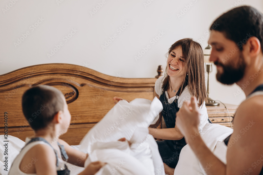 Happy family playing with pillows together on bed. Parents spending free time with their son. Happy family playing with pillows together on bed. Parents spending free time with their son.