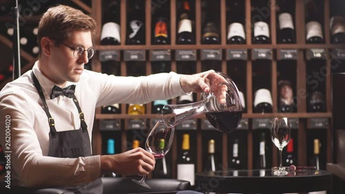 Skilled sommelier pouring wine from decanter into wine glass. Degustation of wine process in wine boutique, close up.