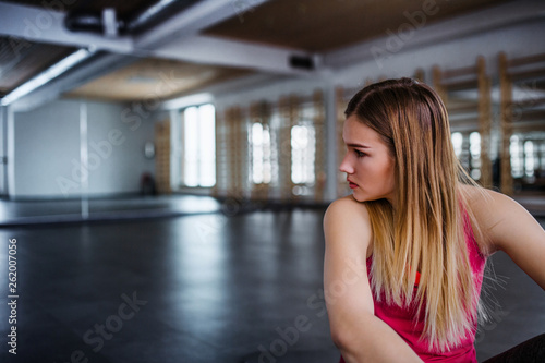 A portrait of young sad and frustrated girl or woman sitting in a gym.