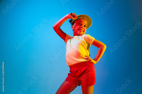 Fototapeta Naklejka Na Ścianę i Meble -  Happy teen girl standing and smiling isolated on trendy blue neon studio background. Beautiful female portrait. Young satisfy girl. Human emotions, facial expression, summer holidays concept.