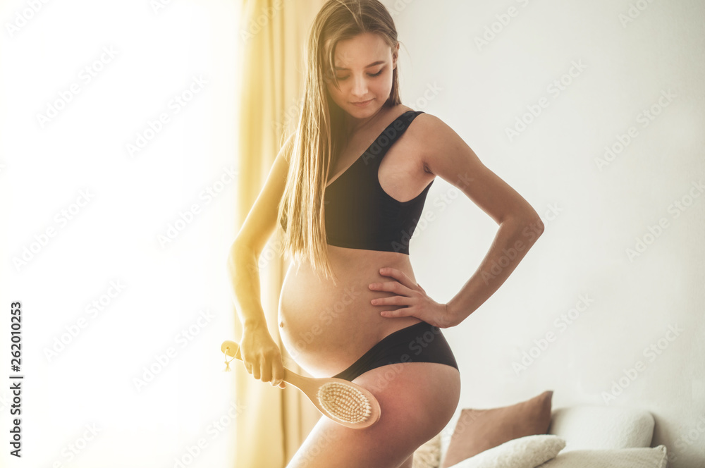 Fototapeta premium Pregnancy and dry massage. Pregnancy Woman holding dry brush to top of her leg. Cellulite treatment, dry brushing
