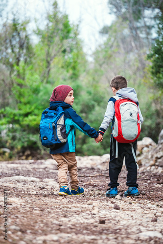 Two boys with backpacks are walking along a forest path.