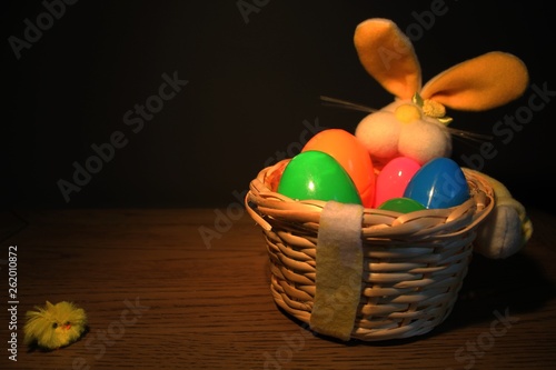 Easter basket with plastic eggs on a wood table. Basket is to the right of the image to allow for text to be placed on the left. There is a small chick on the left of the image. photo