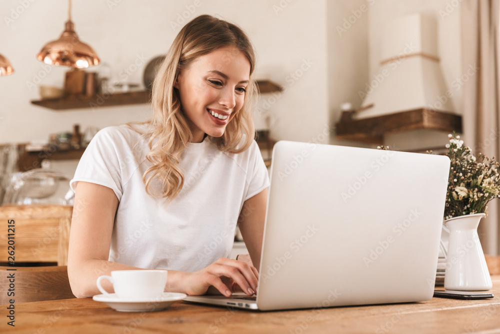 Portrait of young blond woman working on laptop and drinking coffee while sitting in cozy cafe indoor Portrait of young blond woman working on laptop and drinking coffee while sitting in cozy cafe indoor