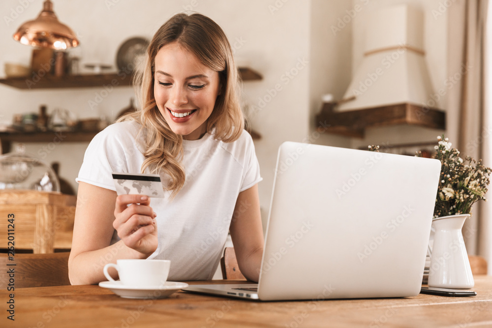Portrait of beautiful blond woman using laptop and credit card for online shopping while sitting in cozy cafe indoor Portrait of beautiful blond woman using laptop and credit card for online shopping while sitting in cozy cafe indoor