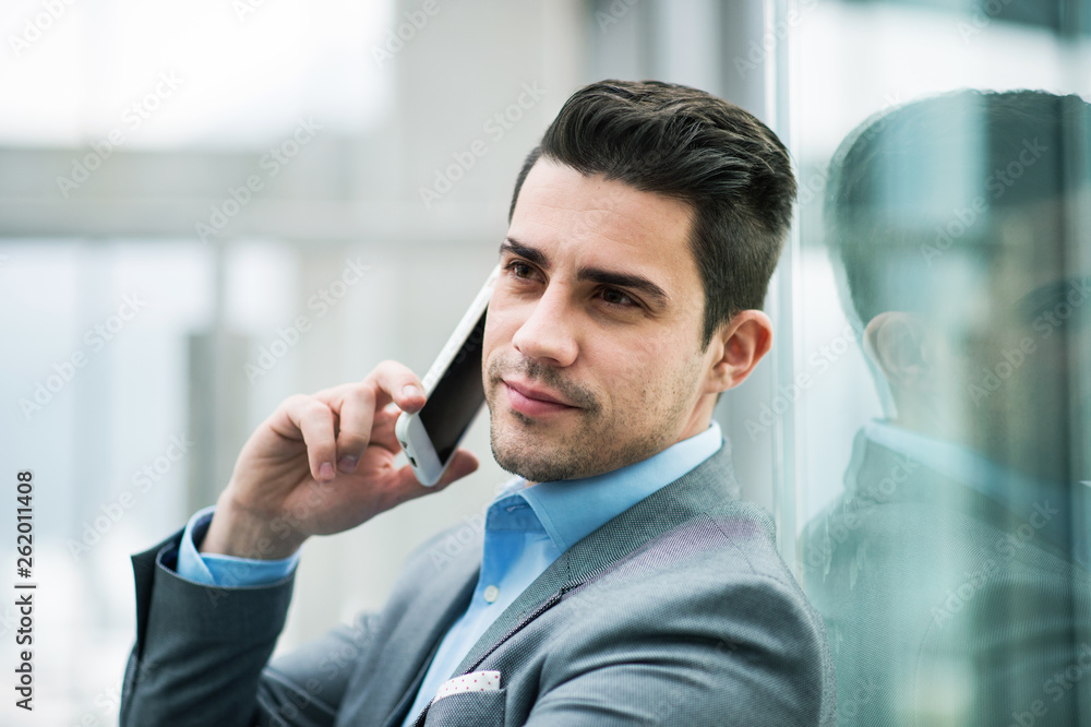 A portrait of young businessman with smartphone sitting in corridor outside office. A portrait of young businessman with smartphone sitting in corridor outside office.