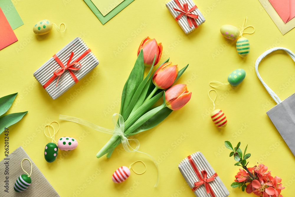 Fototapeta Wielkanocne mieszkanie leżało na żółtym papierze. Bukiet tulipanów, pudełka na prezenty, ozdobne jajka i torby papierowe, układ geometryczny po przekątnej.