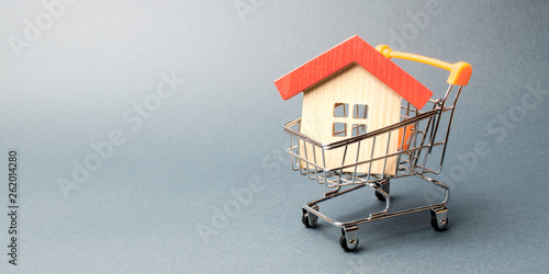 Wooden house in a Supermarket trolley. The concept of buying a house or apartment. Affordable housing. Profitable and cheap loans for real estate. Buying a home. Mortgage and loan. Place for text
