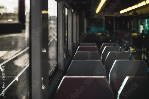 A dark interior of a modern ordinary suburban train in Europe with a row of double chairs, shallow depth of field with selective focus on the foreground, railroad tracks outside the window © skyNext